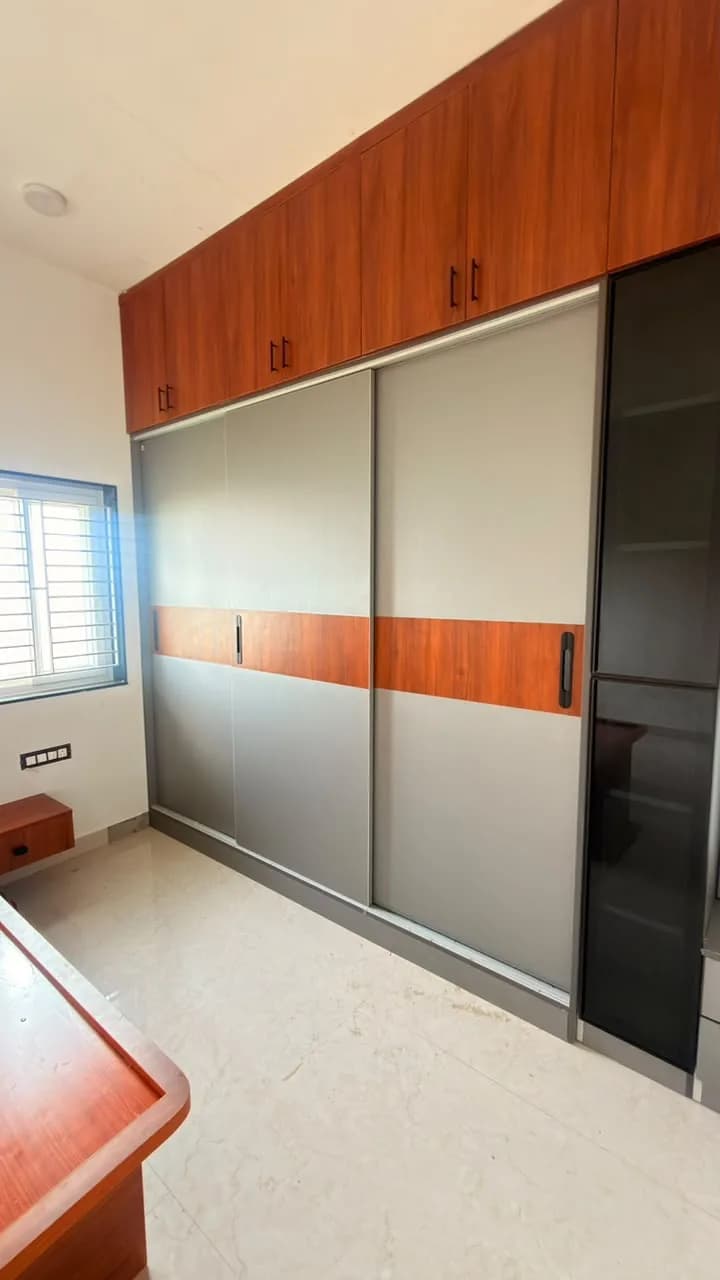 The same bedroom after: a floor-to-ceiling sliding wardrobe with walnut loft cabinets beside the window