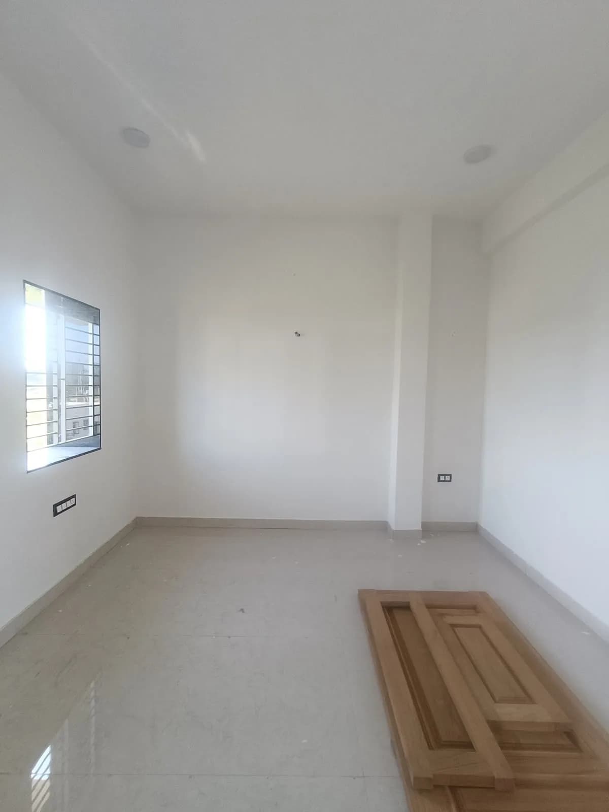The bedroom before: an empty room with bare walls, a window on the left and removed door panels on the floor